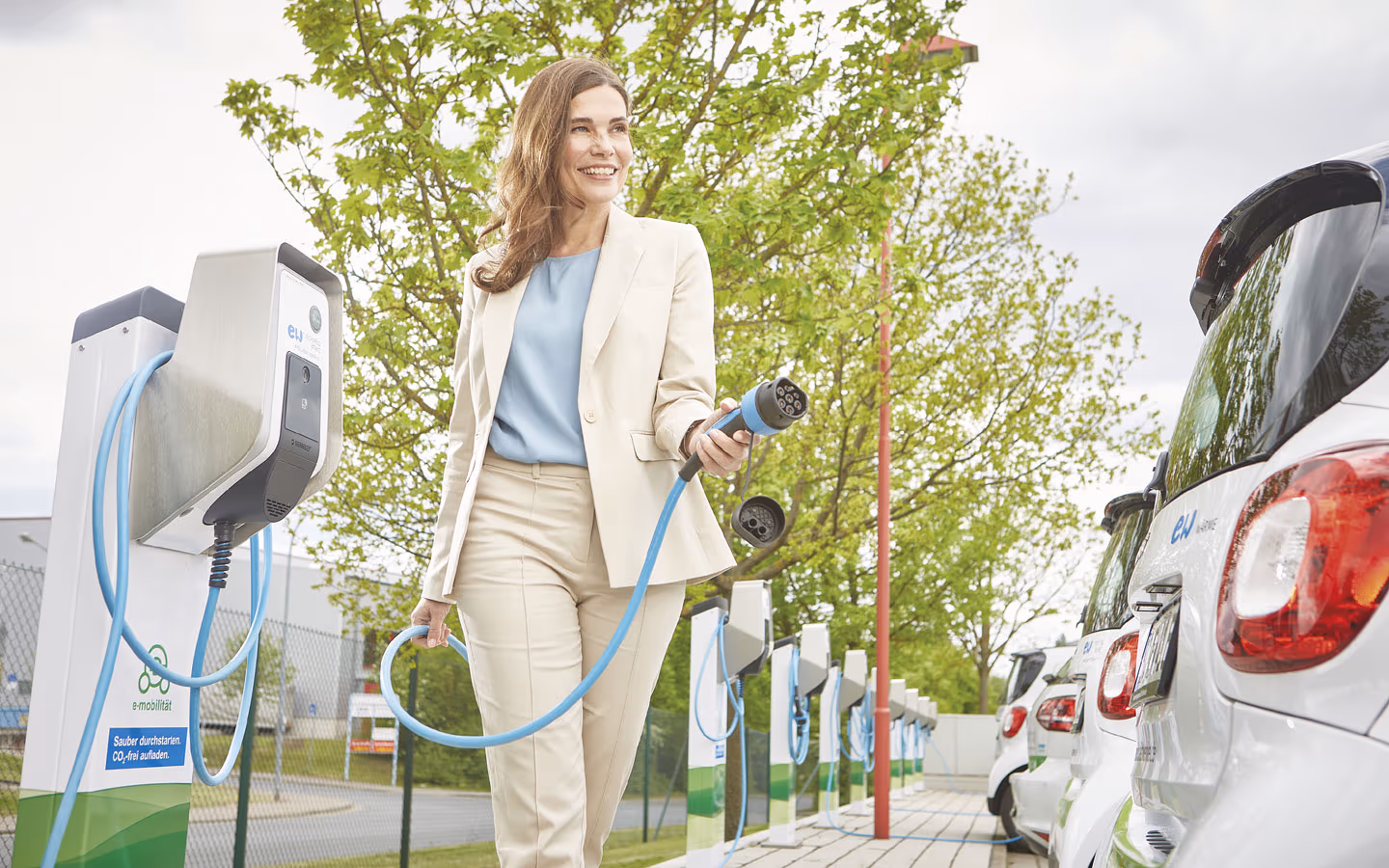E-Mobilität - Kundin vor Ladestation mit Stecker in der Hand &middot; Elektro-Adam-Mühlheim